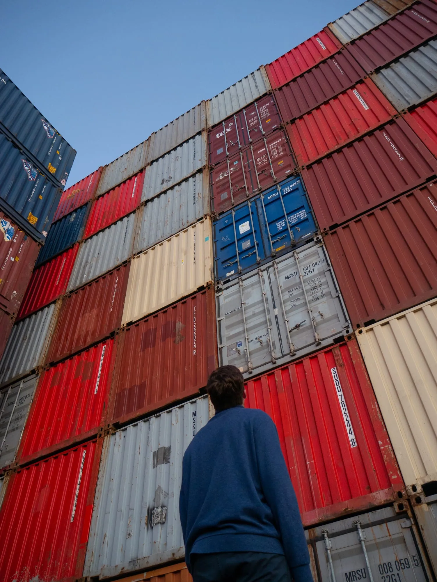 A worker walking past stacked shipping containers