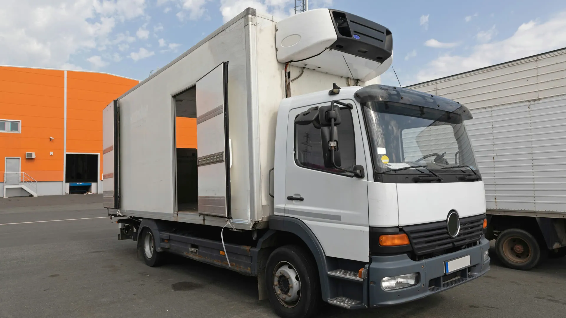White refrigerated truck with its side door open beside a warehouse