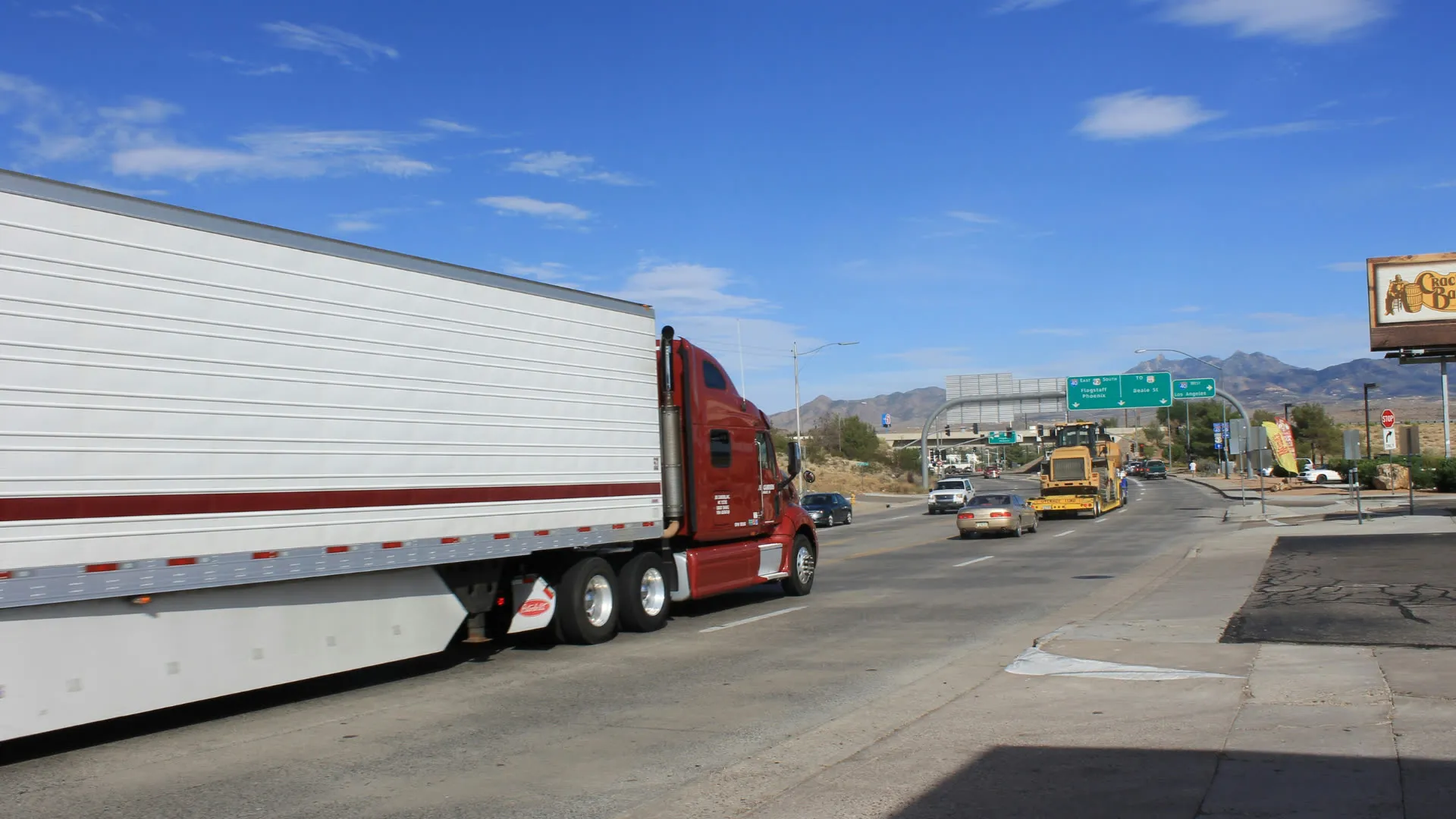 Red semi truck pulling a white trailer on a city highway